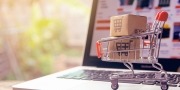 Een laptop die openstaat met een winkelmandje ervoor met een symbool voor online winkelen