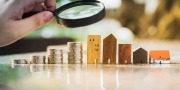 hand met een vergrootglas boven een rij huizen en geld